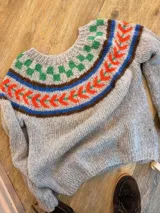 Sweater de punto tejido a mano en lana mohair, de color gris con diseño de guarda geométrica multicolor en el cuello en tonos verde, azul, marrón y naranja.