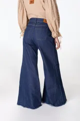 Pantalón de pierna ancha con acabado brillante, confeccionado en lino. Presenta un diseño de tiro medio con cierre de botón y cremallera, bolsillos traseros y etiqueta de marca en la cintura.