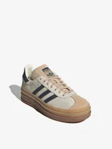 Zapatillas Adidas Gazelle Bold para mujer. Diseño clásico en gamuza color beige con las tres tiras laterales en azul marino. Suela de goma apilada color caramelo.