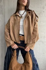 Campera tipo bomber de gamuza con diseño relajado, cierre frontal, cuello camisero y detalles de apliques en los hombros.