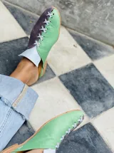 Zapatos tipo mules de punta cerrada y talón abierto, con diseño bicolor que combina cuero metalizado dorado y tono mostaza. Presentan detalles de costuras cruzadas en contraste sobre el empeine y suela baja.