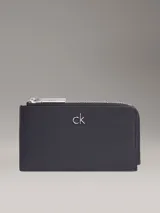 Billetera tipo tarjetero grande de color negro, con cierre en forma de L y logo metálico de la marca en el frente.