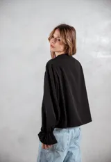 Camisa negra de corte holgado con detalles de bordado tipo broderie en el pecho y mangas largas con puños acampanados.