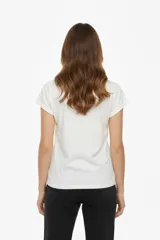 Remera de algodón color verde militar, manga corta con puños doblados y cuello redondo. Presenta un estampado frontal con motivos florales y un fondo con patrón de cuadros en tonos rosados, marrones y verdes.