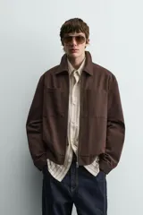 Sobrecamisa de corte regular confeccionada en tejido con estructura canvas color marrón. Presenta un ligero acolchado interior, cuello de solapa y cierre frontal con cremallera metálica. Incluye dos bolsillos de plastrón en el pecho y bolsillos laterales de vivo, con mangas largas terminadas en puños con botón.