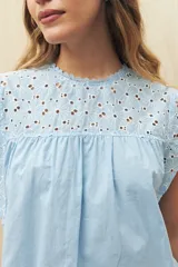 Blusa celeste de manga corta con broderie en el canesú y las mangas. Presenta cuello redondo con terminación de puntilla y recorte fruncido.