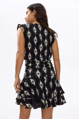 Vestido mini negro sin mangas, con estampado geométrico en tonos blancos, escote redondo fruncido, cintura drapeada y falda escalonada con volados.