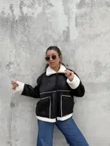 Campera tipo gamulán de color negro con interior y detalles de corderito en color blanco. Presenta cierre frontal, cuello clásico y dos bolsillos frontales.