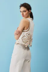 Blusa sin mangas de corte crop en color blanco, con detalles de bordados calados en tono tostado formando diseños florales en el cuello, los hombros y el borde inferior.