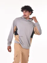 Buzo canguro negro con capucha, diseño de bloques de color en negro, beige y gris claro en el torso y mangas. Presenta un pequeño detalle de texto blanco en el pecho.