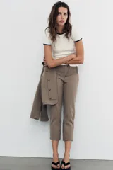 Pantalón capri de tiro medio con raya diplomática en tonos beige y marrón. Presenta trabillas, bolsillos laterales y cierre frontal con cremallera y botón metálico.
