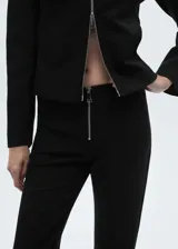 Chaqueta negra de corte recto con cuello camisero y cierre frontal de cremallera doble metálica. Presenta diseño de manga larga y estructura entallada.