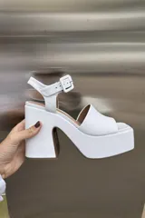 Sandalia de plataforma alta y taco grueso, color blanco, con capellada de cuero y tira de ajuste con hebilla cuadrada en el tobillo.