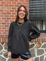 Camisa blanca de manga larga con detalles de encaje o bordado en el canesú y el frente. Presenta un corte holgado y mangas con puños elásticos o fruncidos.