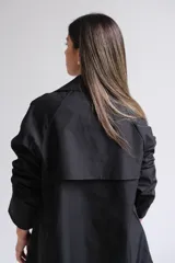 Trench corto de color negro con diseño de doble botonadura, solapas clásicas y corte holgado.