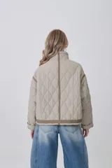 Campera acolchada de diseño capitoné en color beige, con cuello alto, cierre frontal y bolsillos laterales. Presenta un corte holgado con detalles de costuras reforzadas en las mangas y ajuste en la cintura.