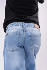 Pantalón de jean tiro bajo con corte wide leg y lavado celeste vintage. Presenta un diseño de pernera ancha y recta, con cierre de botón y cremallera, y bolsillos laterales y traseros.