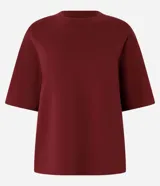 Blusa básica de mujer color negro, confeccionada en malla encorpada de algodón, con cuello redondo y mangas cortas de corte oversized con sisas desplazadas.