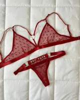 Conjunto de lencería de dos piezas en tul rojo con patrón de corazones y detalles de argollas en forma de corazón. Incluye un bralette triangular con tirantes ajustables y una tanga con la frase "Soy Tuya" aplicada en strass.