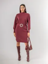 Vestido tipo polerón de tejido de punto color borgoña, con cuello alto, mangas largas con puños ajustados y corte recto. Incluye un cinturón del mismo material con una hebilla decorativa de flor con cristales.
