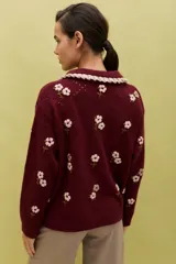 Saco de punto color bordó con bordados artesanales de flores en tonos rosados. Presenta un cuello con detalle de volados en color crema y cierre frontal con botones. De silueta amplia y cómoda.