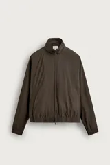 Cazadora bomber de corte relajado, color marrón oscuro, confeccionada en tejido técnico. Cuenta con cuello subido, manga larga amplia, bolsillos de vivo en la cadera, acabados elásticos en puños y ruedo, y cierre frontal con cremallera de doble dirección.