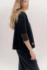 Buzo de punto en color negro con mangas tres cuartos y puños en contraste color marrón. Presenta un diseño holgado con tajos laterales y un aplique circular con logo en la parte inferior.