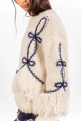 Sweater de punto 100% lana merino en color marfil, de calce holgado y cuello redondo, con detalles bordados en azul marino y flecos decorativos en el bajo y las mangas.