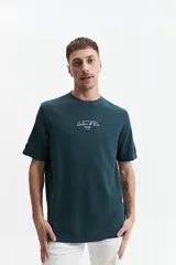 Remera de manga corta, color verde oscuro, con textura tipo waffle o piqué. Presenta un estampado vertical en la espalda con texto en blanco.