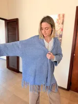 Saco tejido de punto color lavanda con diseño oversize, capucha integrada y detalle de flecos en el ruedo. Presenta mangas amplias y caída relajada.