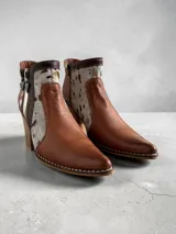 Botas cortas de cuero en tonos marrón y tostado, con paneles de cuero vacuno con estampado animal print tipo ponchada y detalles pintados a mano en dorado. Presentan punta fina, taco cuadrado de madera, costuras visibles a contratono y doble cierre lateral con tiradores metálicos personalizados.