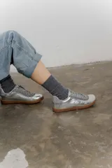 Zapatillas bajas de cuero color crema con detalles en marrón y cordones blancos.