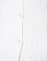 Cardigan blanco de tejido liviano con trama en relieve, cuello a la base y cierre frontal con botones a tono. Presenta mangas tres cuartos.