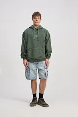 Canguro de algodón con efecto lavado de corte oversize, capucha con cordones ajustables, bolsillo canguro delantero y estampa frontal con texto en el pecho.