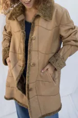 Campera tipo gamulán de cuero genuino en color marrón, con interior y detalles en corderito sintético color crema. Presenta cierre frontal con botones, cuello solapa y puños con vuelta.