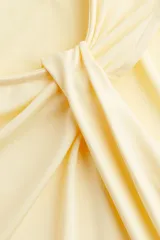 Top sin mangas de punto elástico color amarillo pálido, con ajuste entallado y detalle de nudo o drapeado asimétrico en el hombro derecho.