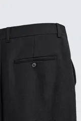 Pantalón de corte recto confeccionado en tejido de lana. Presenta bolsillos frontales, bolsillos traseros de vivo con botón y cierre frontal con cremallera y botón.