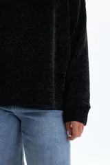 Sweater de tejido chenille en color negro, con cuello redondo, mangas largas y puños acanalados. Presenta una textura suave y un corte holgado.
