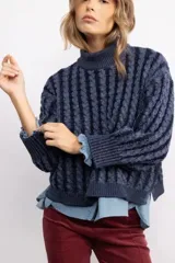 Sweater de tejido de punto con diseño de trenzas verticales, cuello alto y corte oversize. Presenta una textura marcada y puños acanalados.