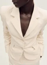 Blazer de corte recto y diseño estructurado, confeccionado en una mezcla de algodón y lino. Presenta cuello con solapas de muesca, cierre frontal con botones, mangas largas con puños abotonados y dos bolsillos laterales con solapa. Incluye forro interior y abertura posterior en el bajo.