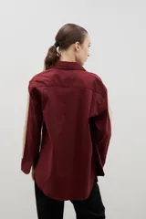 Camisa de corte holgado y largo medio, color negro con detalle de franja lateral en color crema a lo largo de las mangas. Presenta cuello clásico, cierre frontal con botones y tajos laterales en el ruedo.