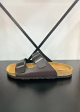 Sandalias marrones de ecocuero con doble tira y hebillas plateadas ajustables.