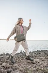 Cartera tipo bucket de cuero gamuzado color verde oliva, con correa de hombro y correa bandolera ajustable. Tiene dos bolsillos externos, cierre con broche imán y forro interno de gabardina de algodón con tres compartimentos.