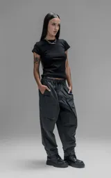 Pantalón de estilo utilitario confeccionado en textil técnico ripstop color gris oscuro. Presenta un corte oversize con cintura elástica, cierre frontal con broche técnico, bolsillos delanteros de gran tamaño con cierre y sistema de ajuste en los tobillos mediante broches snap.