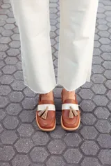 Mocasines de cuero color tostado, con detalle de antifaz en cuero crudo y borlas decorativas. Hechos a mano en Uruguay.