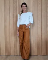 Pantalón de jean color tostado, de corte ancho y tiro alto. Presenta costuras verticales decorativas en el frente, bolsillos laterales y cierre frontal con botón. El diseño incluye un acabado desflecado en el ruedo.