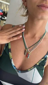Collar de mostacillas de acrílico color turquesa con un dije colgante en forma de cuerno italiano (cornicello) rojo con incrustaciones de piedras turquesas. El engarce del dije y las cuentas separadoras son de metal dorado.