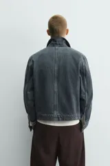 Cazadora cropped fit de denim de algodón, color negro lavado. Presenta cuello solapa, manga larga con puños abotonados, cierre frontal de cremallera y bolsillo superior con cierre de cremallera en el pecho.