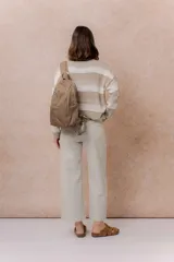Mochila compacta de color beige, con compartimento principal con cierre, bolsillos laterales y bolsillo frontal con cierre oculto. Cuenta con correas regulables y acolchonadas y asa superior.