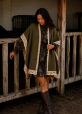Ruana de lana merino y mohair color verde oliva, con diseño de caída fluida y terminaciones artesanales de encaje tejido en color crema en los bordes.